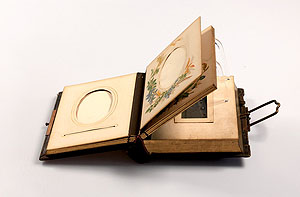 Fotoalbum mit leeren Passepartout-Seiten. Im unteren Block eine Süieluhr. Foto: Erkenbert-Museum Frankenthal. 